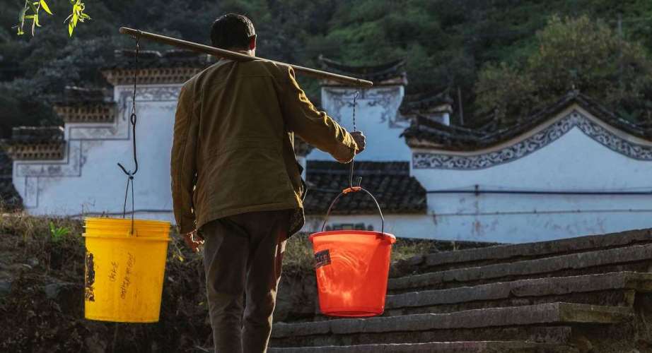 Man carrying buckets on shoulder