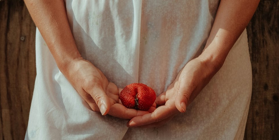 Woman holding strawberry in her hand in front of her body
