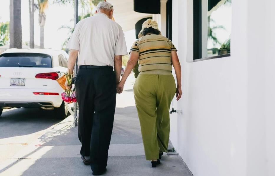 Two older adults walking hand in hand on pavewalk