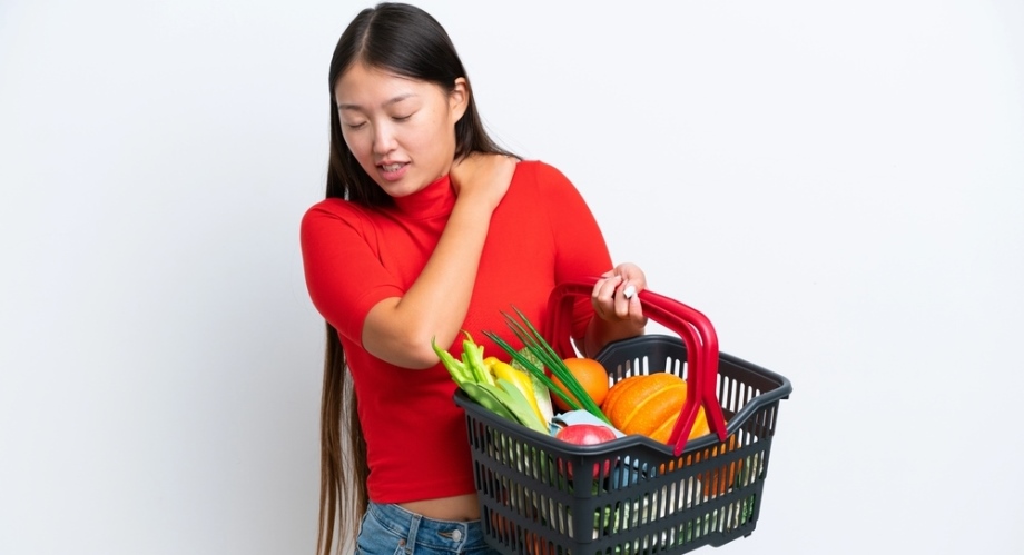 Young woman carrying groceries with pain in her shoulder